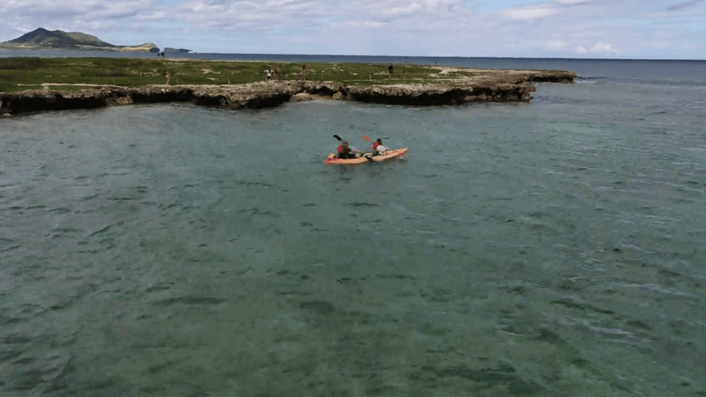 Two people paddle a tandem kayak rental from Active Oahu in front of Popoia Island